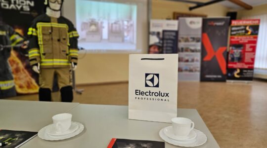 Aussicht von einem Sitzplatz auf die projezierte Powerpoint-Präsentation. Im Vordergrund Kaffeetassen (leer :( ) und eine Goody-Bag mit dem Logo von Electrolux