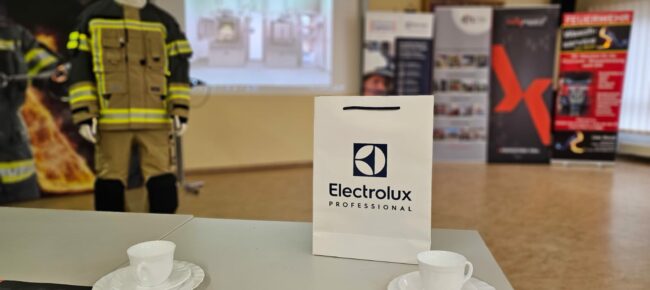 Aussicht von einem Sitzplatz auf die projezierte Powerpoint-Präsentation. Im Vordergrund Kaffeetassen (leer :( ) und eine Goody-Bag mit dem Logo von Electrolux